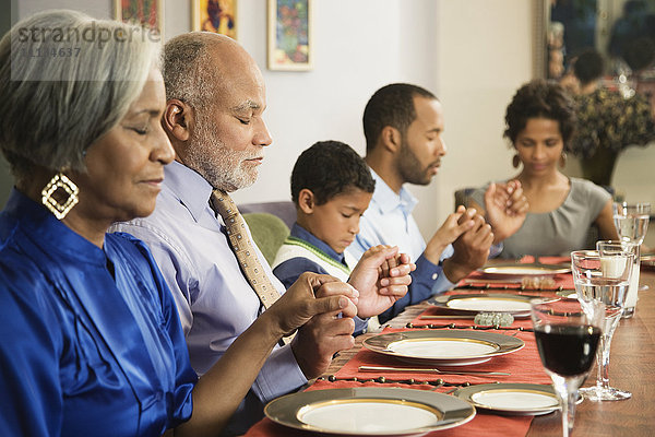 Afroamerikanische Familie spricht am Esstisch das Tischgebet