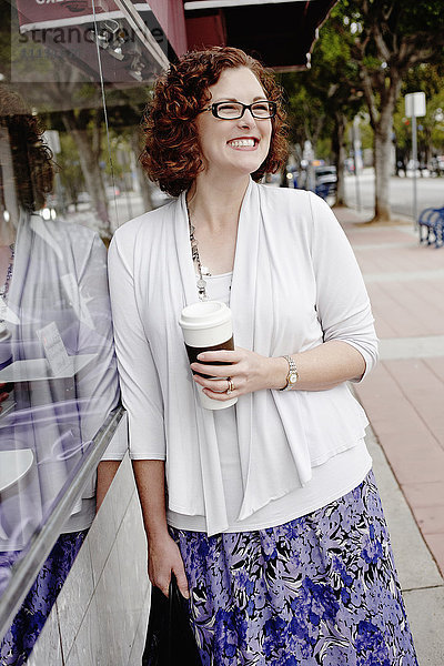 Gemischtrassige Frau trinkt Kaffee auf dem Bürgersteig
