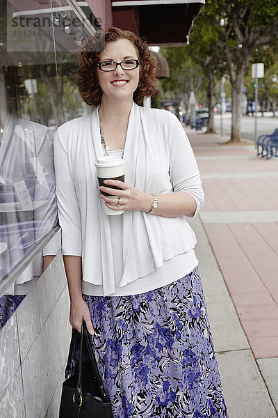 Gemischtrassige Frau trinkt Kaffee auf dem Bürgersteig