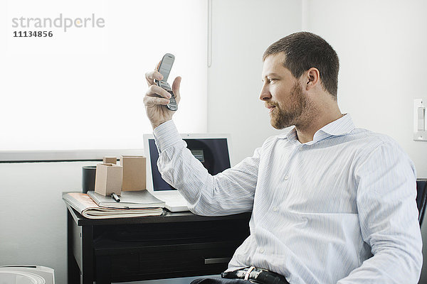 Kaukasischer Geschäftsmann  der ein Mobiltelefon am Schreibtisch benutzt