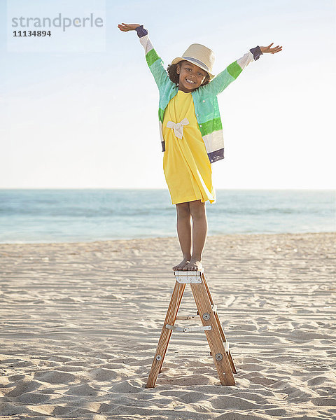 Gemischtrassiges Mädchen steht auf einer Leiter am Strand