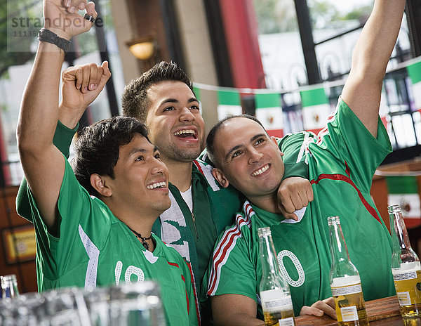 Jubelnde hispanische Männer beim Fernsehen in einer Sportbar