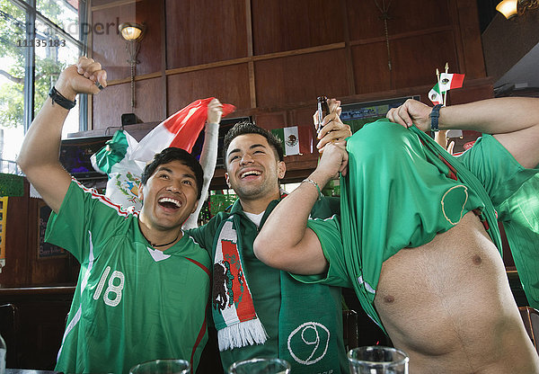 Jubelnde hispanische Männer beim Fernsehen in einer Sportbar