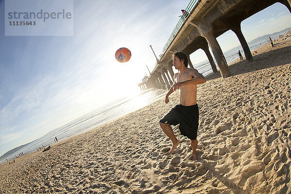 Hispanischer Mann spielt mit Fußball am Strand