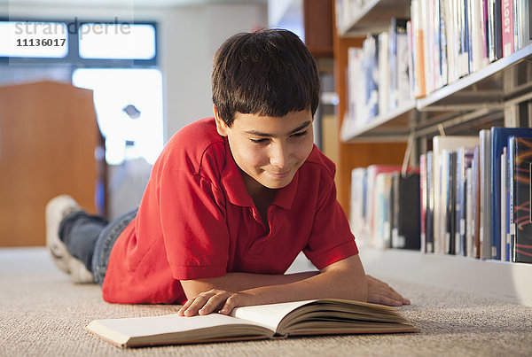 Hispanischer Junge liest ein Buch in der Bibliothek
