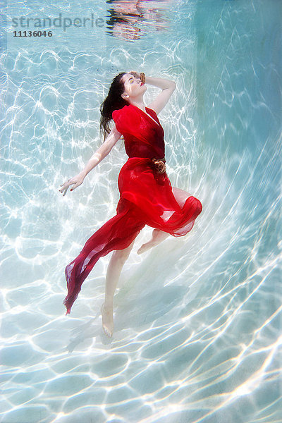 Gemischtrassige Frau im Kleid unter Wasser im Schwimmbad