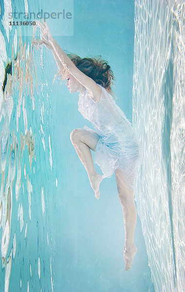 Gemischtrassige Frau im Kleid unter Wasser im Schwimmbad