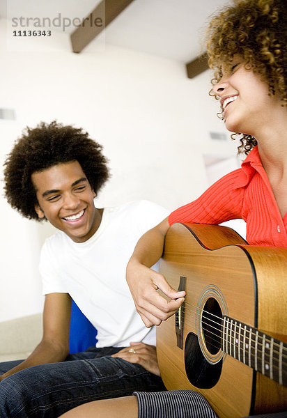 Mann hört seiner Freundin beim Gitarrenspiel zu