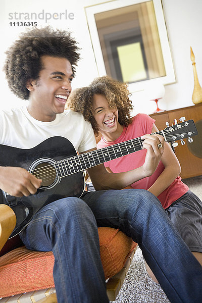 Frau lacht  während ihr Freund Gitarre spielt