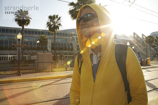 Gemischtrassige Frau mit Kapuze und Sonnenbrille beim Spaziergang