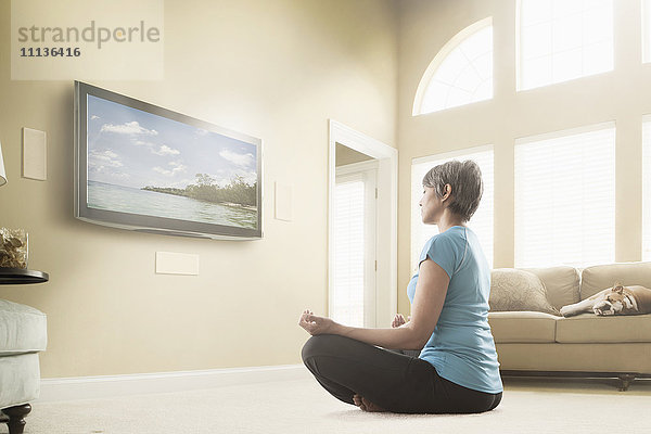 Gemischtrassige Frau sieht sich Meditationsprogramm im Fernsehen an