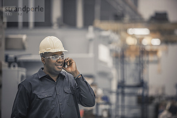 Afroamerikanischer Arbeiter benutzt Mobiltelefon in einer Fabrik