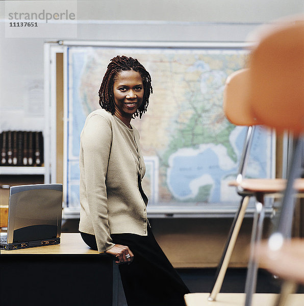 Afroamerikanischer Lehrer sitzt am Schreibtisch im Klassenzimmer