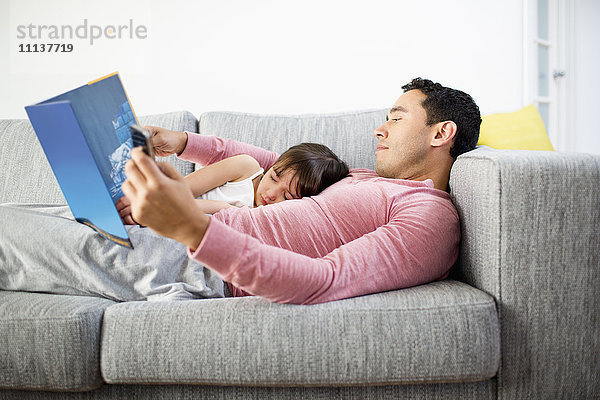 Vater und Tochter lesen gemeinsam auf dem Sofa