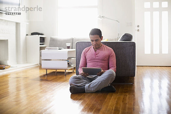 Gemischtrassiger Mann benutzt digitales Tablet im Wohnzimmer