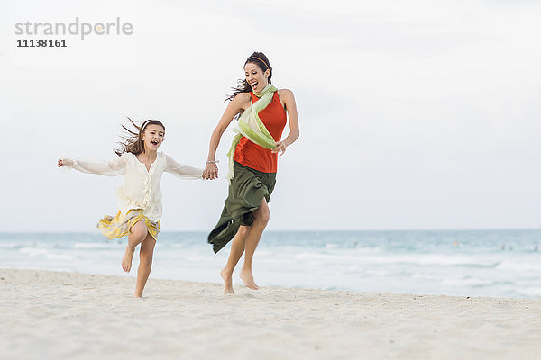 Hispanische Mutter und Tochter laufen am Strand