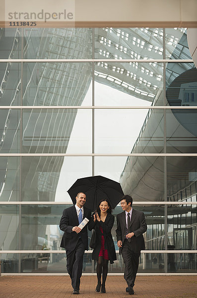 Geschäftsleute gehen zusammen mit Regenschirm