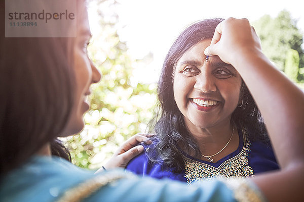 Indische Frau legt Schmuckstück auf die Stirn ihrer Mutter