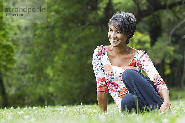 Lächelnde gemischtrassige Frau auf einem Feld sitzend