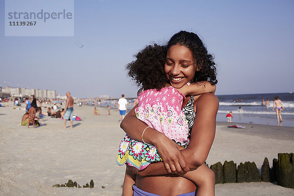 Gemischtrassige Mutter und Tochter umarmen sich am Strand