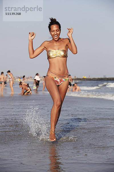 Gemischtrassige Frau watet am Strand im Meer