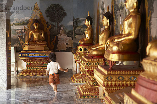 Gemischtrassiges Kind läuft an Buddha-Statuen vorbei