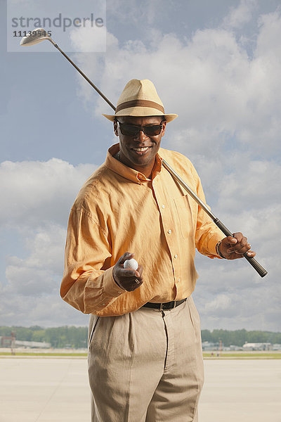 Afroamerikanischer Golfer mit Schläger und Ball auf dem Asphalt