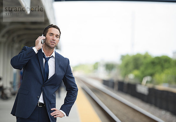Kaukasischer Geschäftsmann  der auf dem Bahnsteig mit einem Handy telefoniert