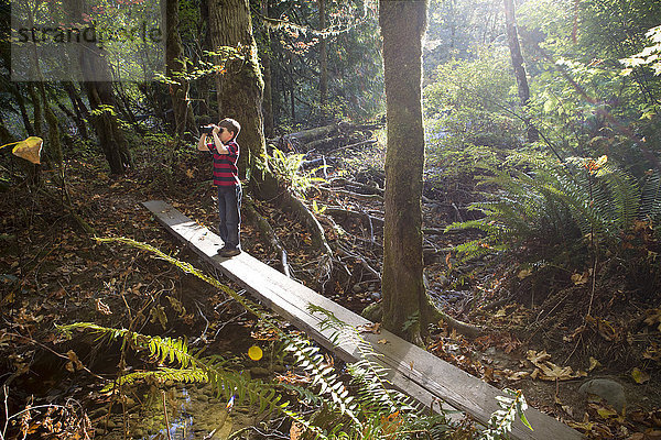 Kaukasischer Junge auf Brücke mit Fernglas im Wald