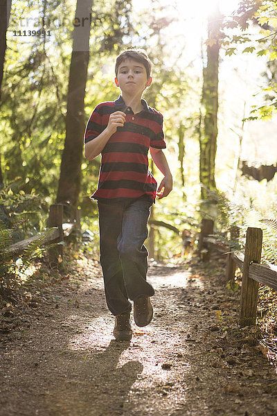 Kaukasischer Junge läuft auf einem Pfad im Wald