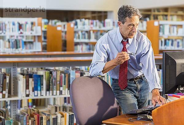 Älterer Mann arbeitet am Computer in einer Bibliothek