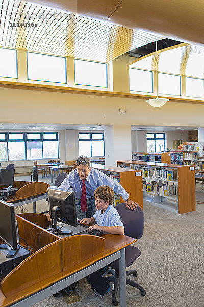 Lehrer und Schüler arbeiten am Computer in der Bibliothek