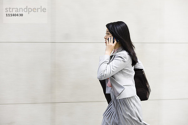 Chinesische Geschäftsfrau  die spazieren geht und mit einem Handy telefoniert