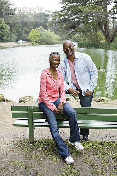 Afroamerikanisches Paar sitzt auf einer Bank in der Nähe eines Sees