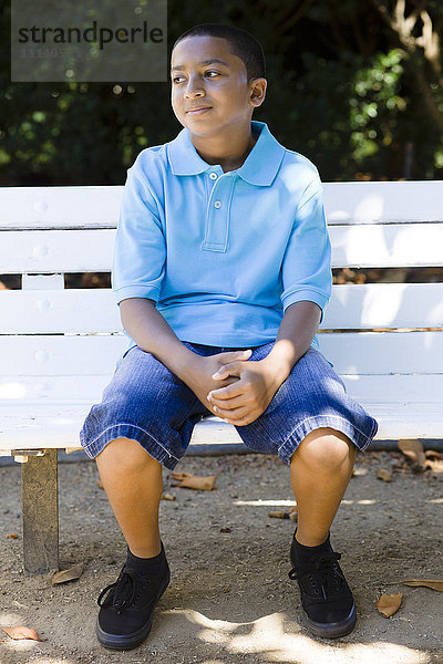 Lächelnder Junge gemischter Rasse sitzt im Park