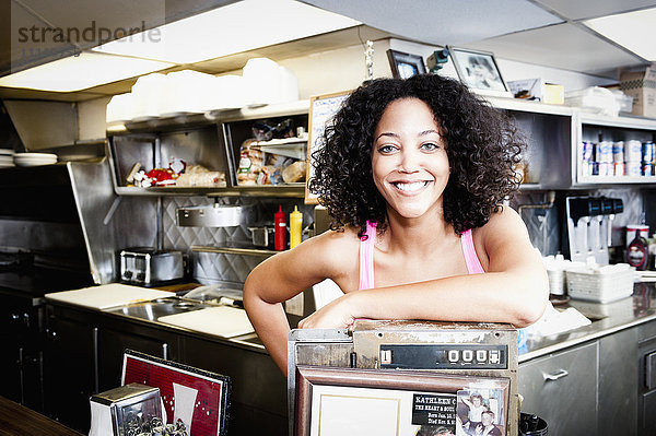 Lächelnde afroamerikanische Frau lehnt sich in einem Diner an die Kasse