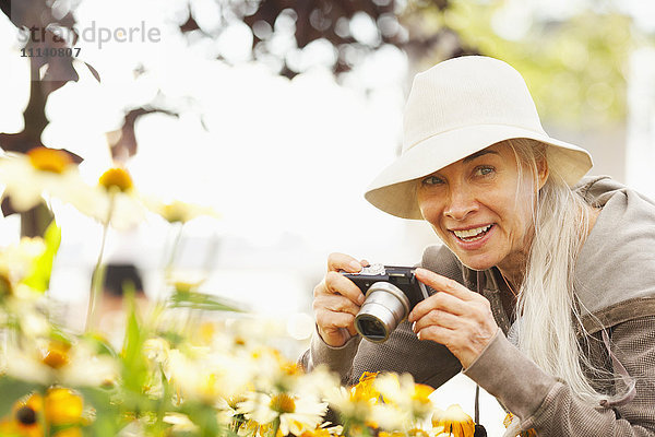 Lächelnde kaukasische Frau  die mit einer Digitalkamera Blumen fotografiert