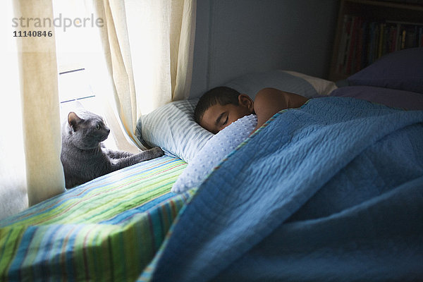 Gemischtrassiger Junge schläft im Bett mit Katze