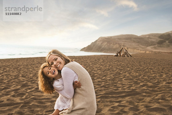 Lächelnde Mutter und Tochter umarmen sich am Strand