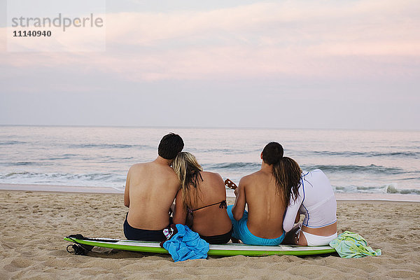 Teenager-Pärchen sitzt auf einem Surfbrett am Strand