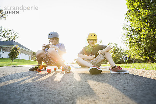 Weiße Jungen sitzen auf Skateboards und benutzen Handys