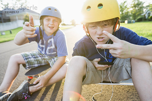 Kaukasische Jungen sitzen auf Skateboards und machen Gesten