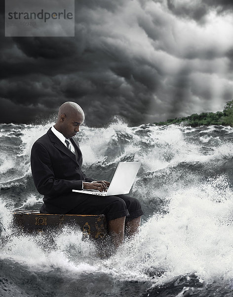 Afroamerikanischer Geschäftsmann benutzt Laptop in stürmischer See