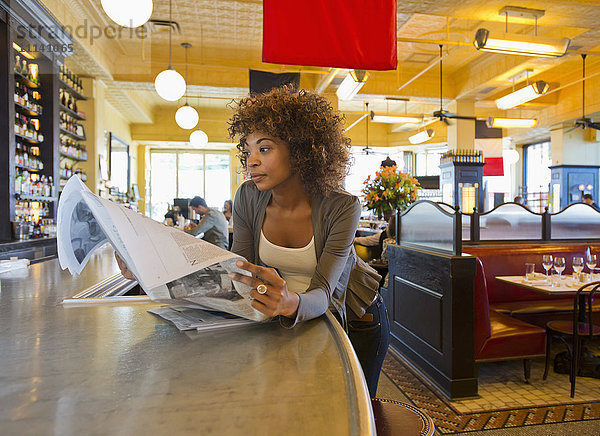 Afroamerikanische Frau liest in einem Café Zeitung