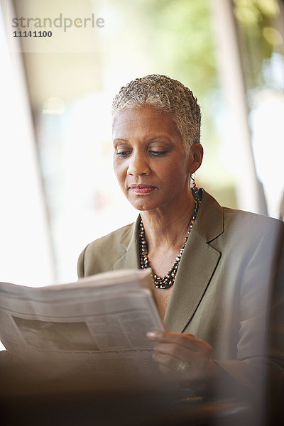Afroamerikanische Geschäftsfrau liest in einem Café Zeitung