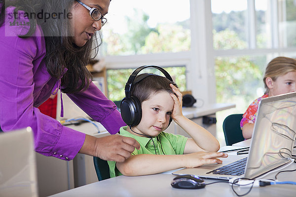 Lehrer hilft einem Schüler bei der Benutzung eines Laptops im Klassenzimmer