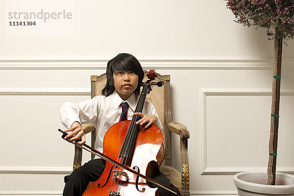 Vietnamesischer Junge spielt Cello auf einem eleganten Stuhl