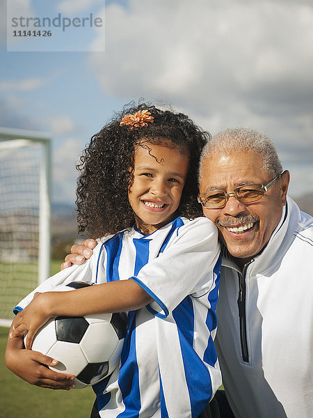 Mann lächelt mit Enkelin auf Fußballplatz