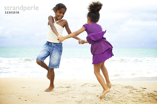 Gemischtrassige Schwestern halten sich an den Händen und spielen am Strand