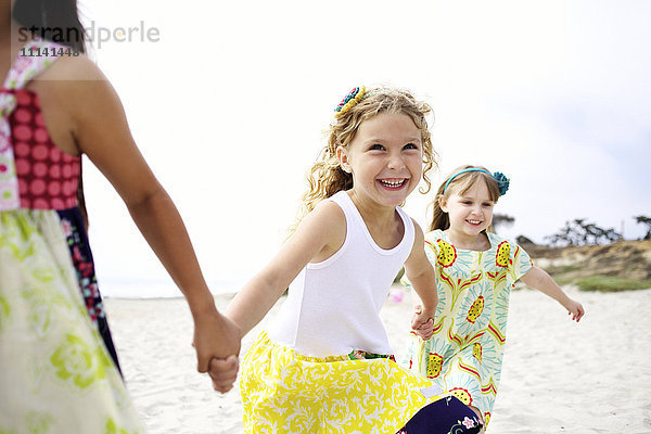 Kinder halten sich an den Händen und laufen am Strand